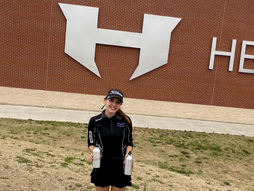 A girl holding two water bottles near a wall
